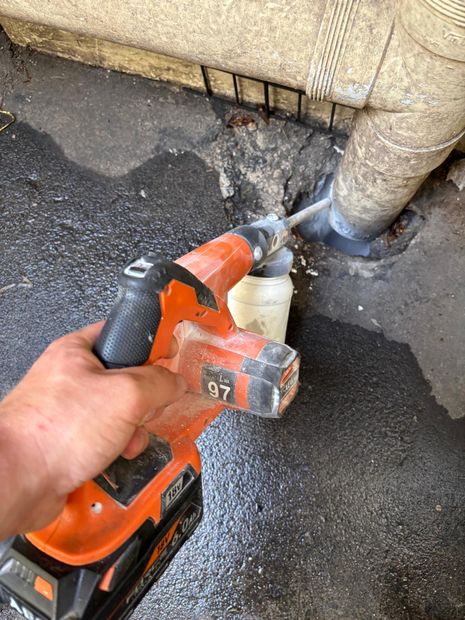 Technician applying insecticidal dust into the gap around a pipe penetration at the rear of a Manly cafe