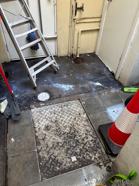 Rear service yard of the cafe after residual treatment, showing the grease trap access cover and floor waste